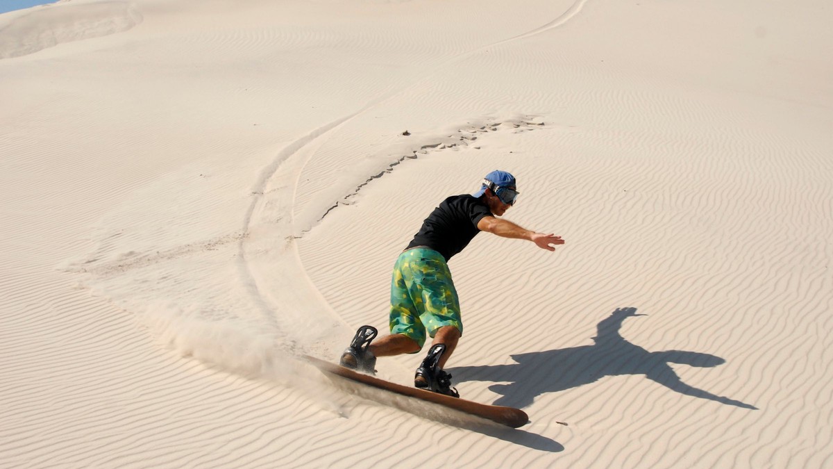 beginner riding a sandboard down a coastal dune near Agadir